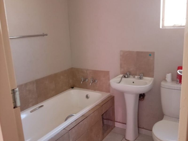 A functional bathroom featuring a bathtub, pedestal basin, and toilet with neutral tiled finishes, requiring minor cosmetic updates to improve its overall presentation.
