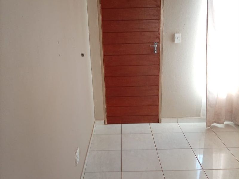 A simple, empty bedroom featuring neutral wall tones, tiled flooring, and a wooden door, providing a clean canvas for personalization.