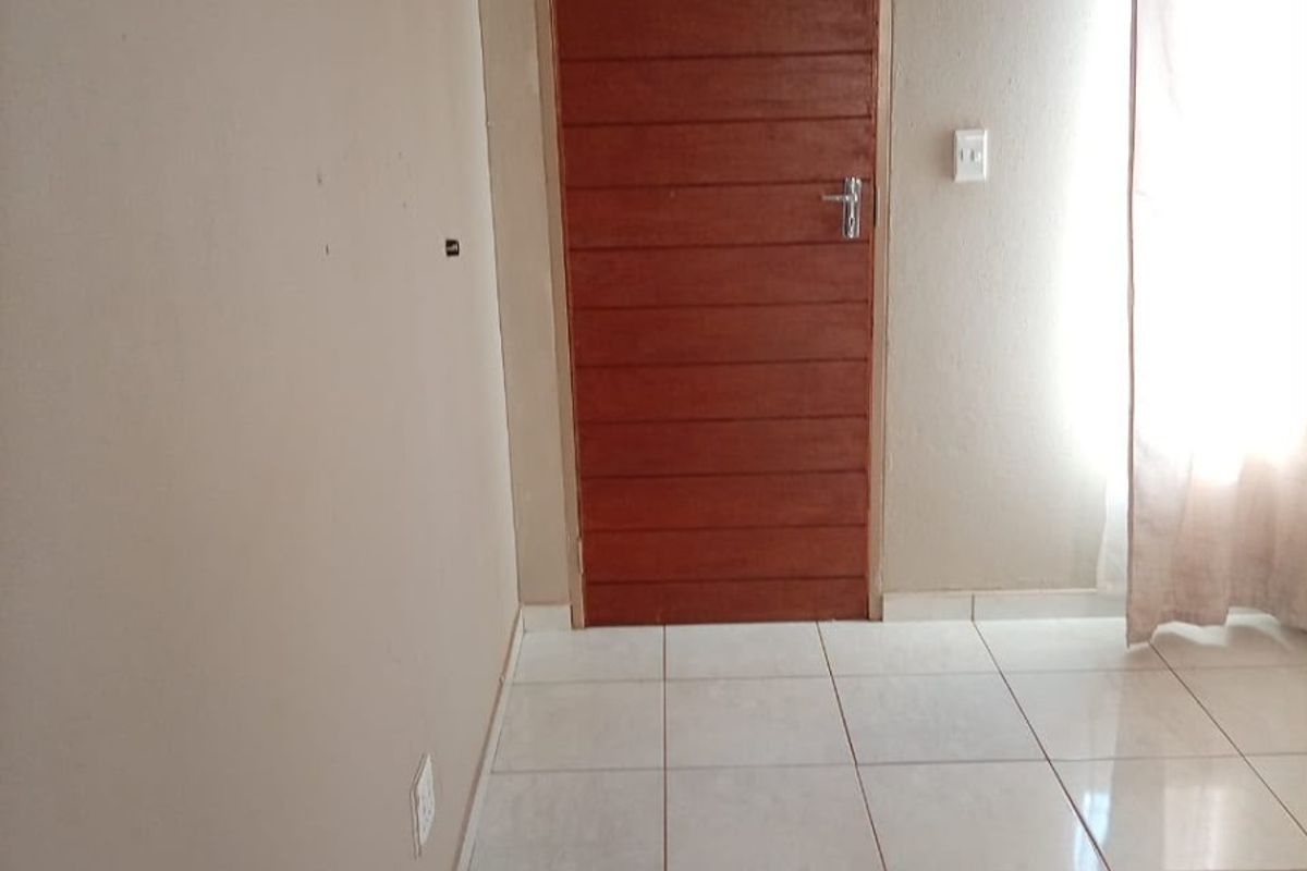 A simple, empty bedroom featuring neutral wall tones, tiled flooring, and a wooden door, providing a clean canvas for personalization.