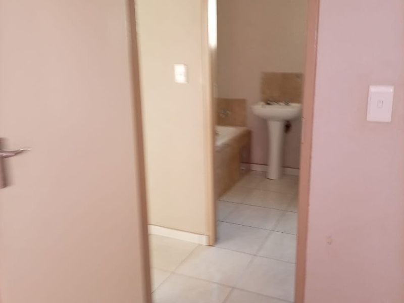 A view through a doorway into a simple bathroom featuring a pedestal basin and a built-in bathtub with tiled flooring.