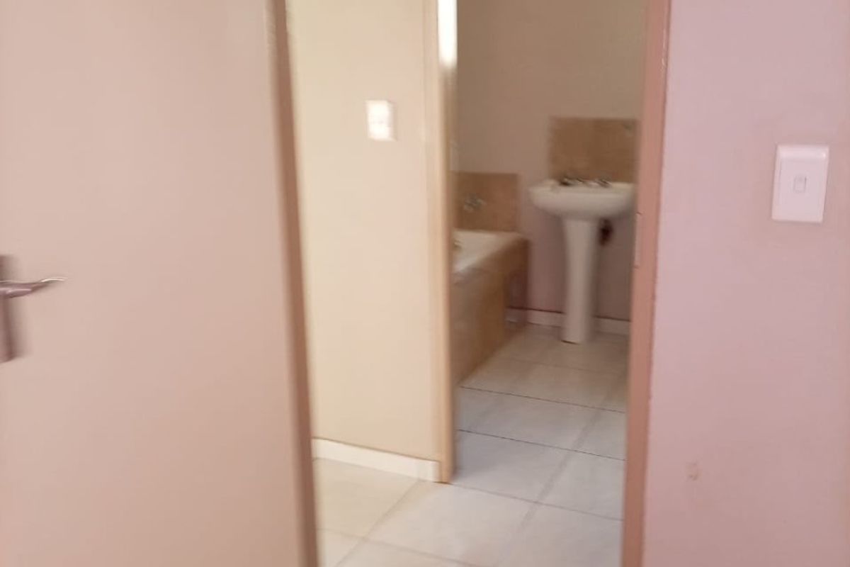 A view through a doorway into a simple bathroom featuring a pedestal basin and a built-in bathtub with tiled flooring.