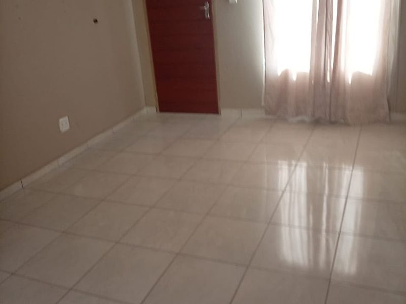 An empty living room featuring neutral wall paint, light-colored floor tiles, and a single internal door.