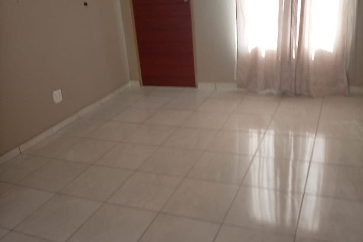 An empty living room featuring neutral wall paint, light-colored floor tiles, and a single internal door.