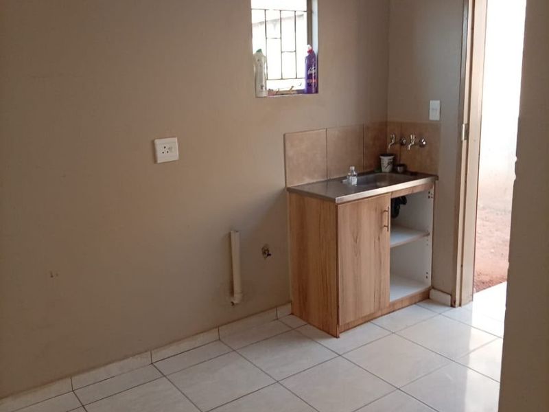A functional laundry area featuring ceramic floor tiles, a stainless steel sink with built-in cabinetry, and a small window with security bars.