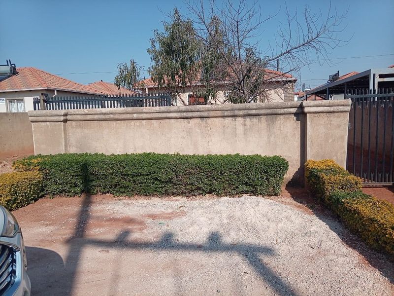Front exterior view featuring a gravel driveway, perimeter wall, and established hedging, providing a basic entrance area to the property.