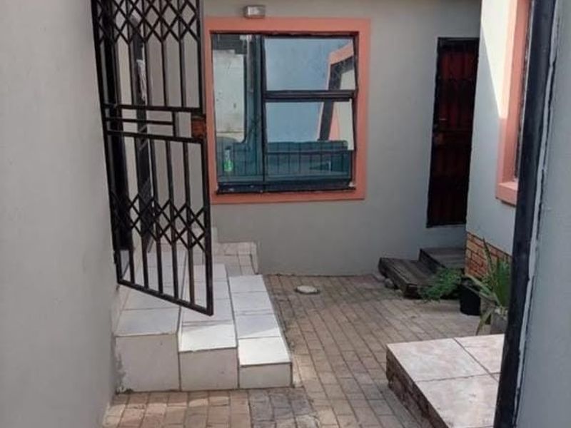 A paved rear courtyard area featuring a security gate, tiled steps, and an overhead awning, providing access to the property's rear entrance.