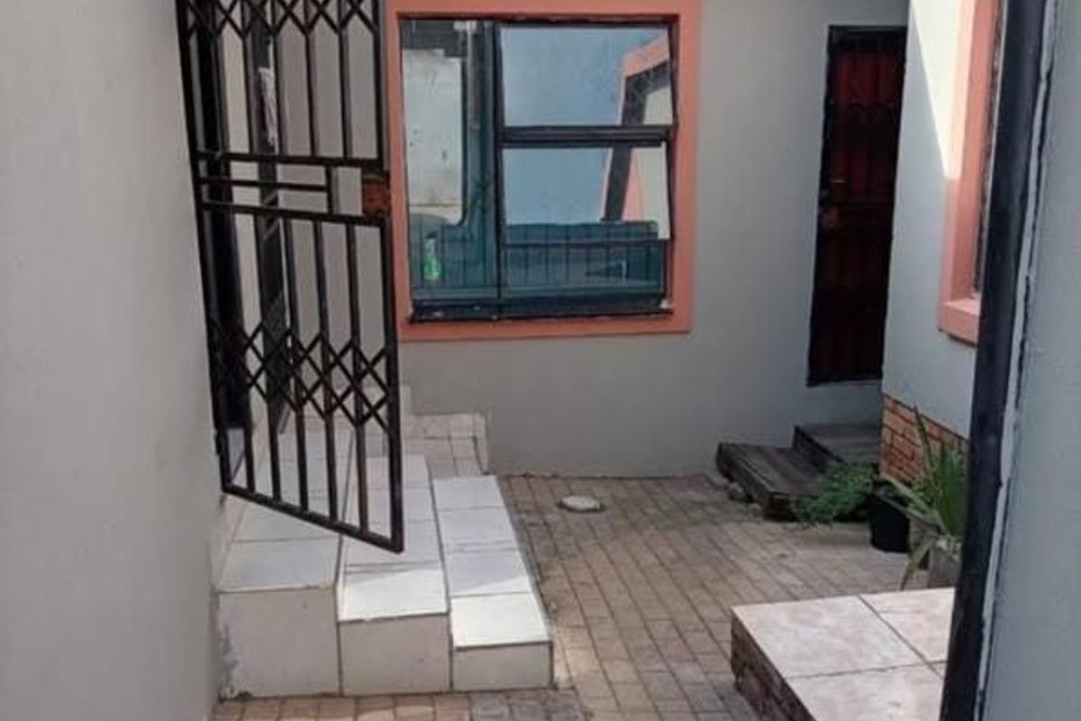 A paved rear courtyard area featuring a security gate, tiled steps, and an overhead awning, providing access to the property's rear entrance.