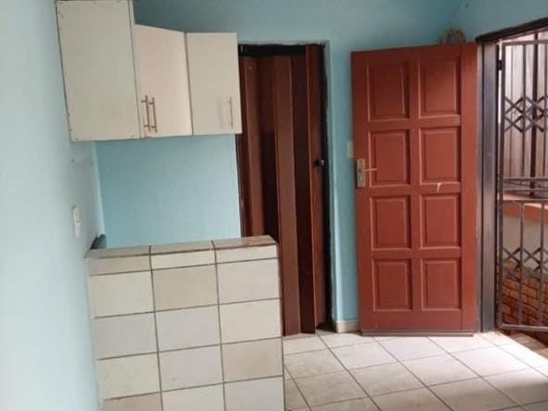 A compact kitchen area featuring tiled counter space, wall-mounted cabinetry, and direct access to an exterior security gate.