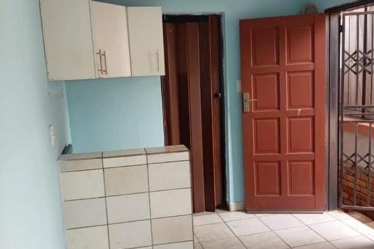 A compact kitchen area featuring tiled counter space, wall-mounted cabinetry, and direct access to an exterior security gate.