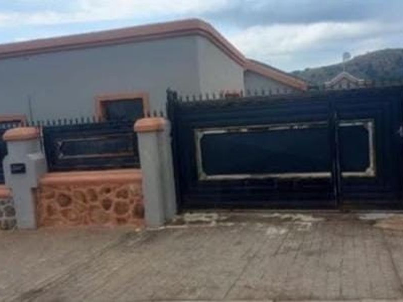 Front view of the property featuring a secure metal driveway gate, stone-clad perimeter wall, and concrete driveway.