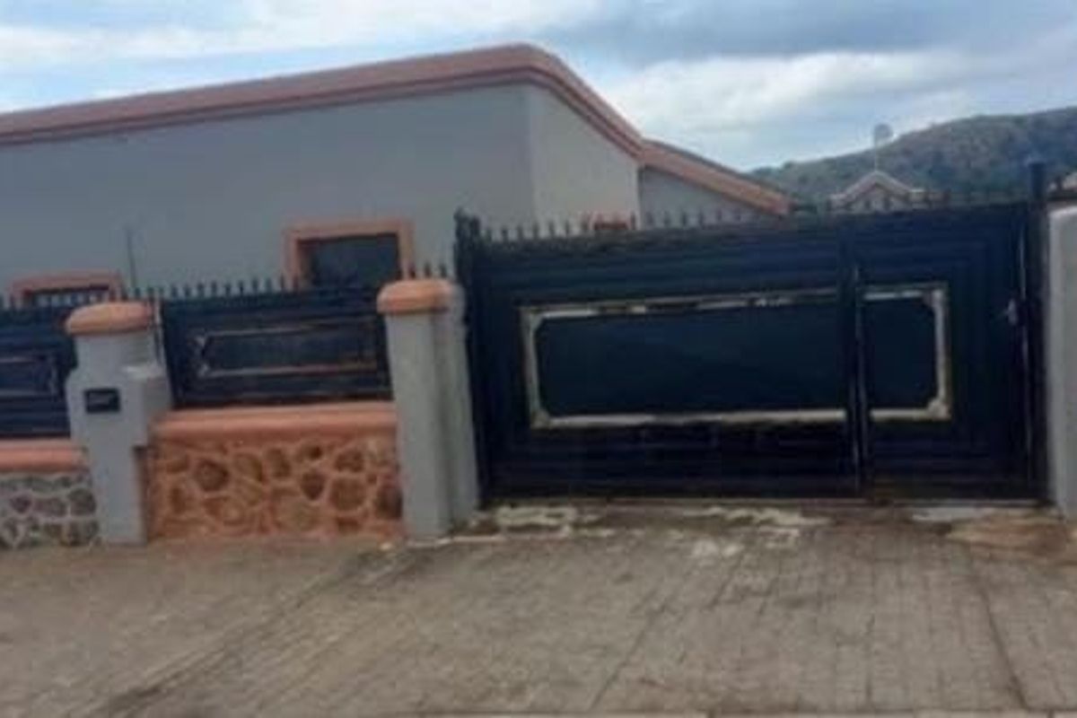 Front view of the property featuring a secure metal driveway gate, stone-clad perimeter wall, and concrete driveway.