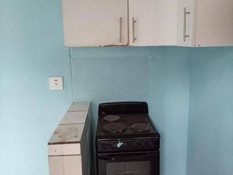 A compact kitchen area featuring basic white cabinetry, a freestanding electric stove, and tiled flooring, requiring cosmetic updates to improve its overall condition.