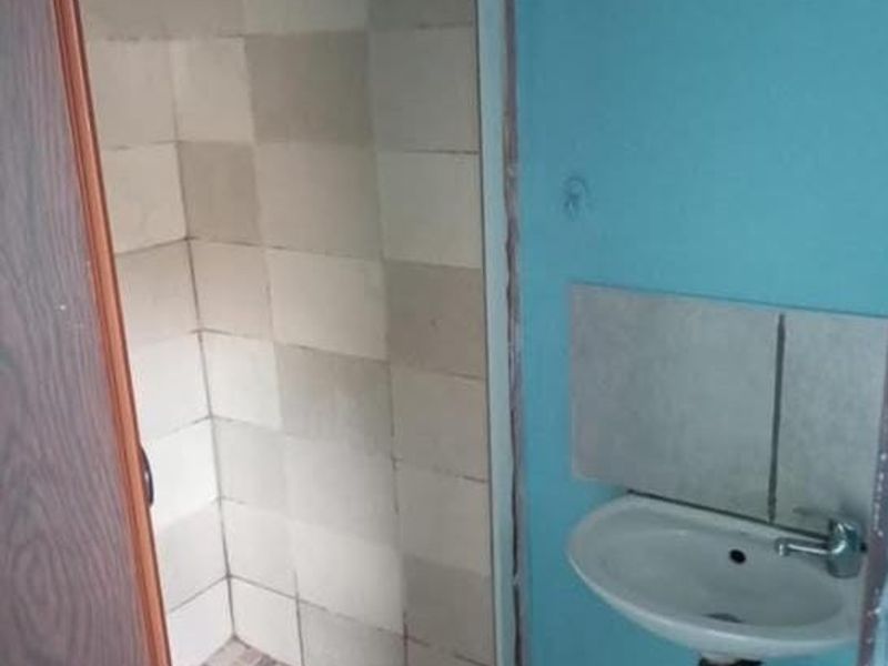 A small, basic bathroom featuring a wall-mounted basin with exposed plumbing and a tiled shower enclosure.