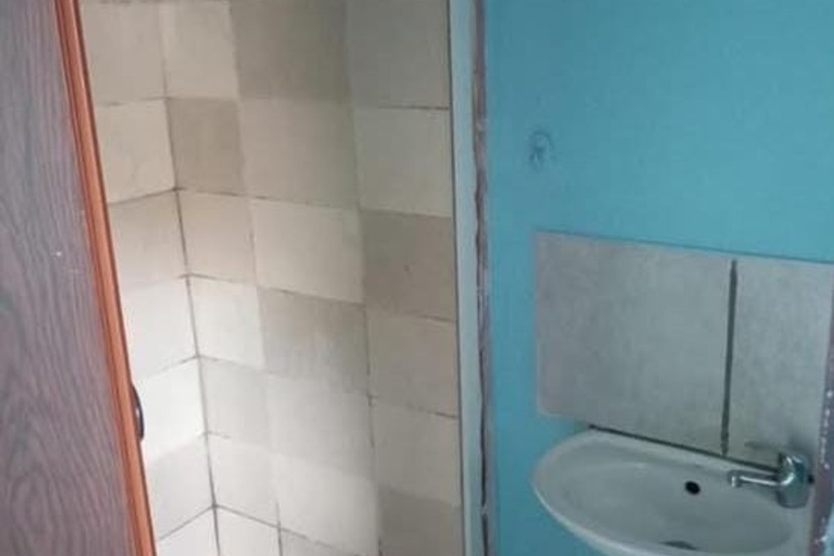 A small, basic bathroom featuring a wall-mounted basin with exposed plumbing and a tiled shower enclosure.