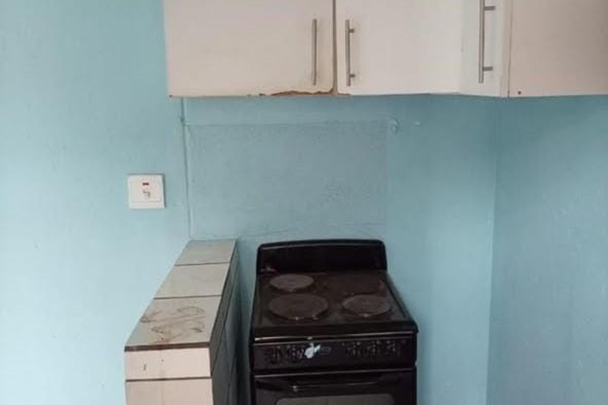 A compact kitchen area featuring basic white cabinetry, a freestanding electric stove, and tiled flooring, requiring cosmetic updates to improve its overall condition.