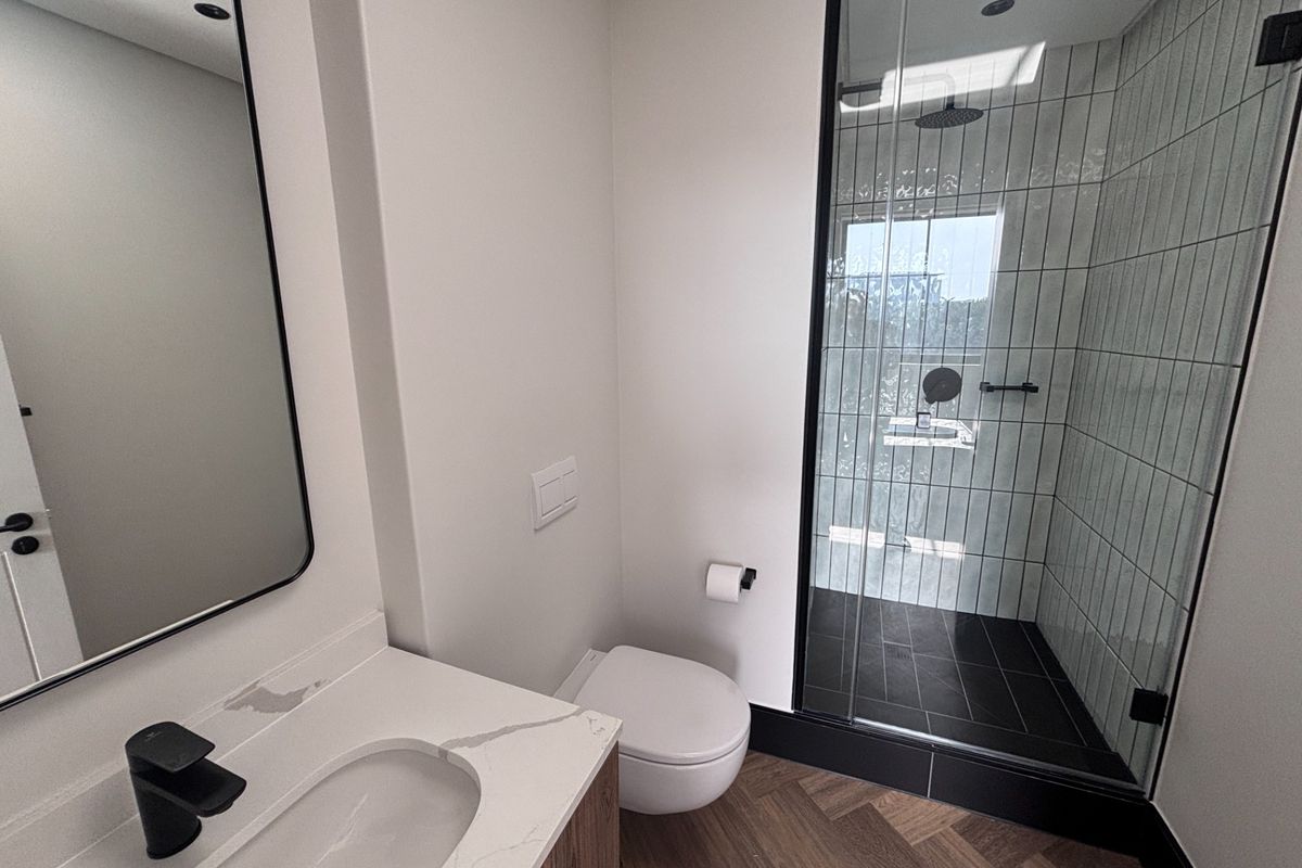 Modern bathroom featuring a glass-enclosed shower with rain head, wall-hung toilet, and a sleek vanity with stone countertop and black matte fixtures.