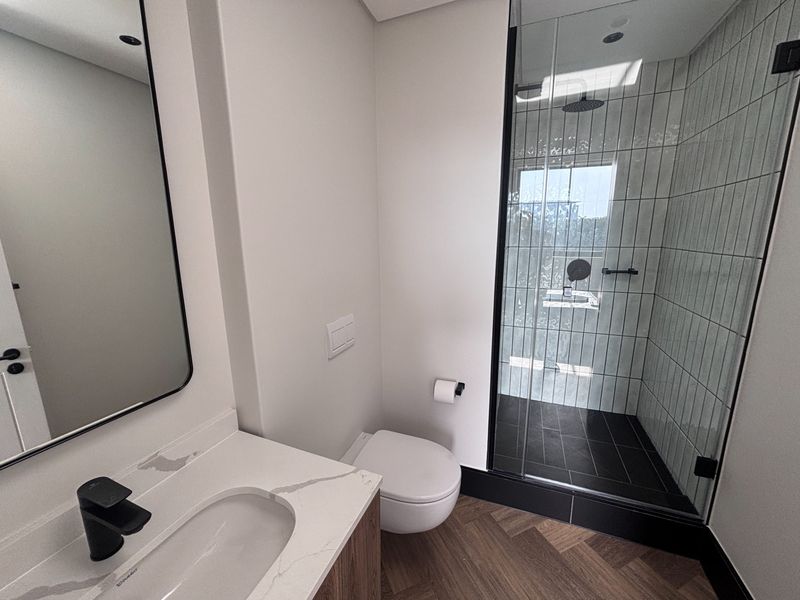 Modern bathroom featuring a glass-enclosed shower with rain head, wall-hung toilet, and a sleek vanity with stone countertop and black matte fixtures.