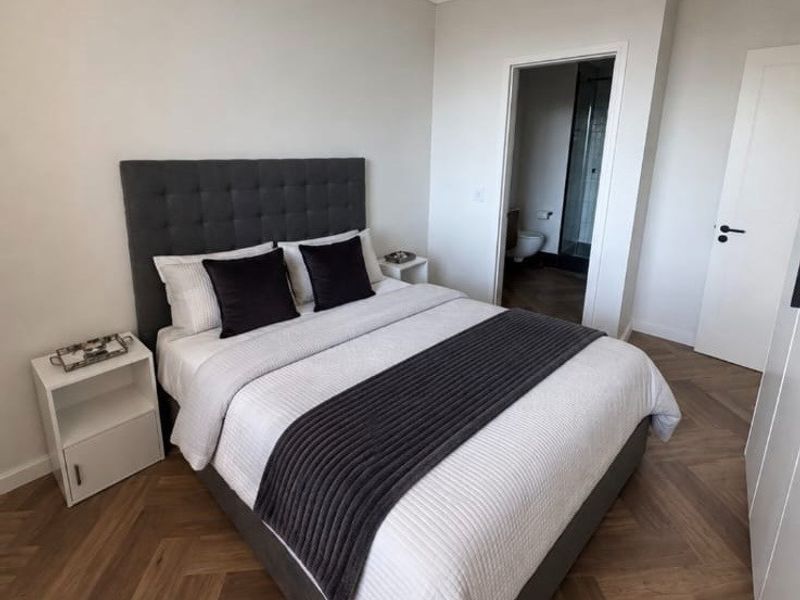 A modern bedroom featuring elegant herringbone timber flooring, neutral walls, and direct access to an en-suite bathroom.