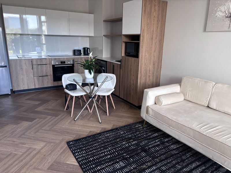 Modern open-plan living area featuring high-quality herringbone flooring, sleek two-tone kitchen cabinetry, and integrated appliances in a well-maintained apartment setting.