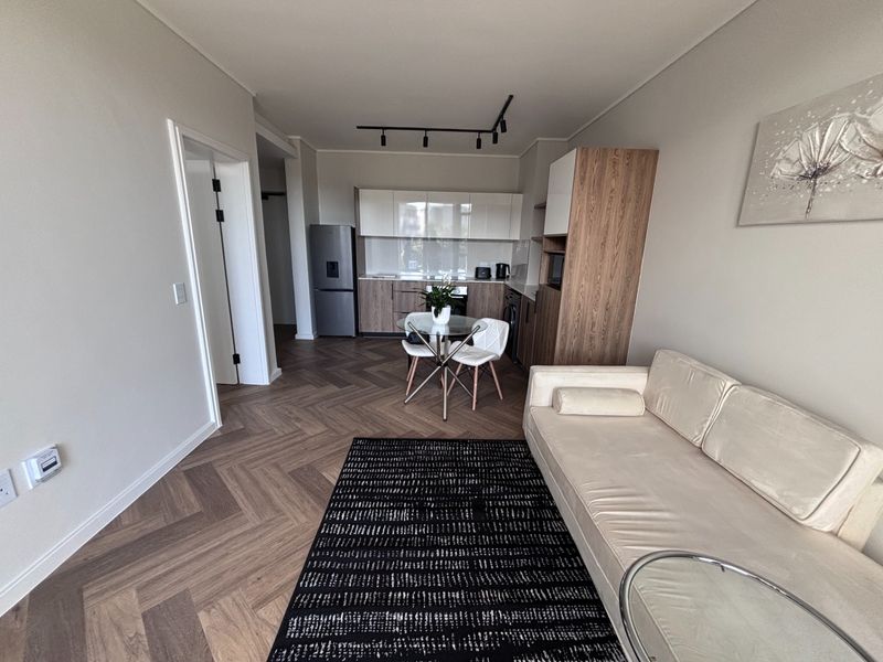 Modern open-plan living area featuring high-quality herringbone timber flooring, contemporary kitchen cabinetry, and sleek track lighting in a well-maintained apartment setting.