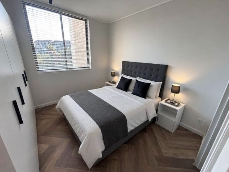 A modern, well-maintained bedroom featuring stylish herringbone flooring, a large built-in wardrobe, and venetian blinds for privacy.