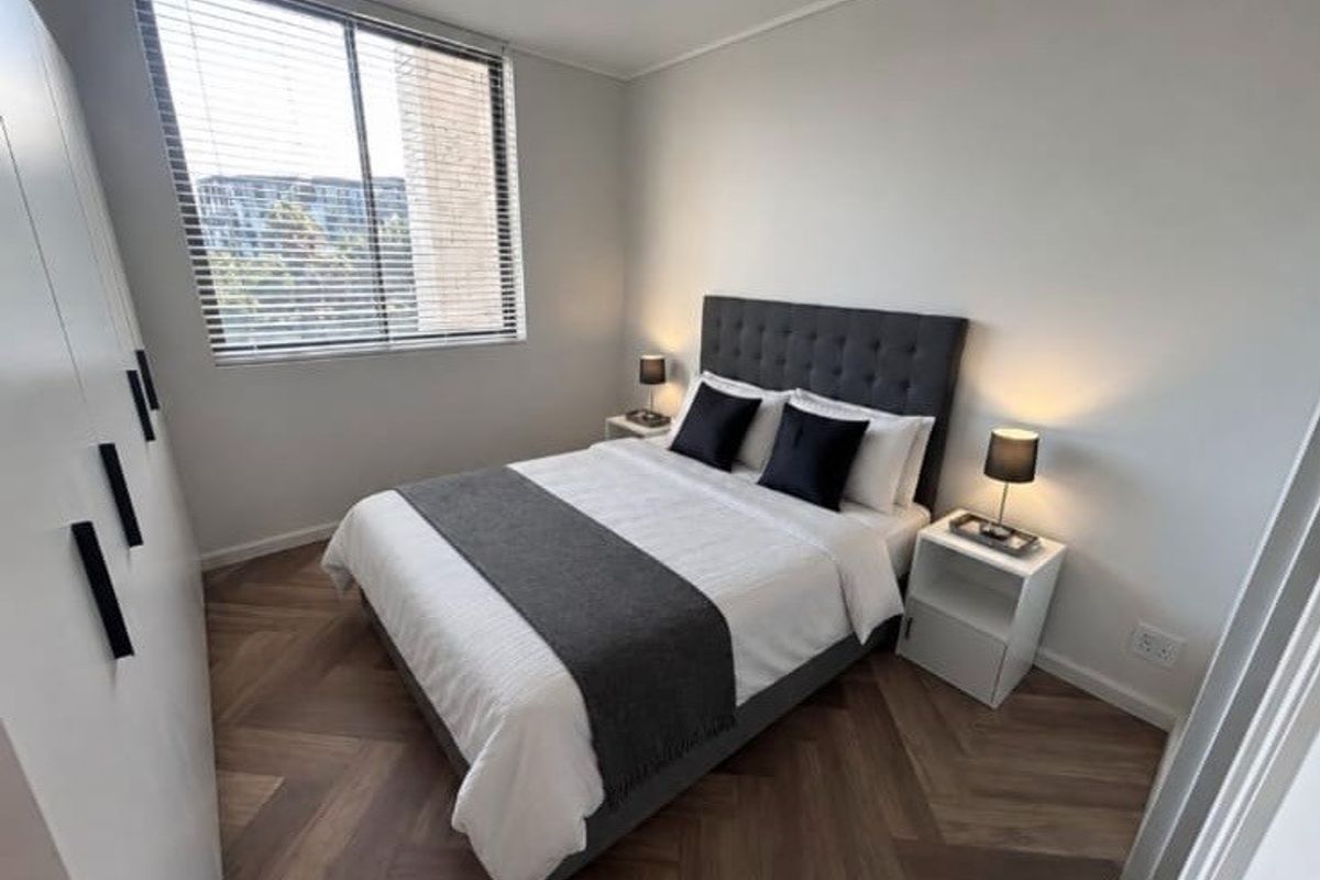 A modern, well-maintained bedroom featuring stylish herringbone flooring, a large built-in wardrobe, and venetian blinds for privacy.