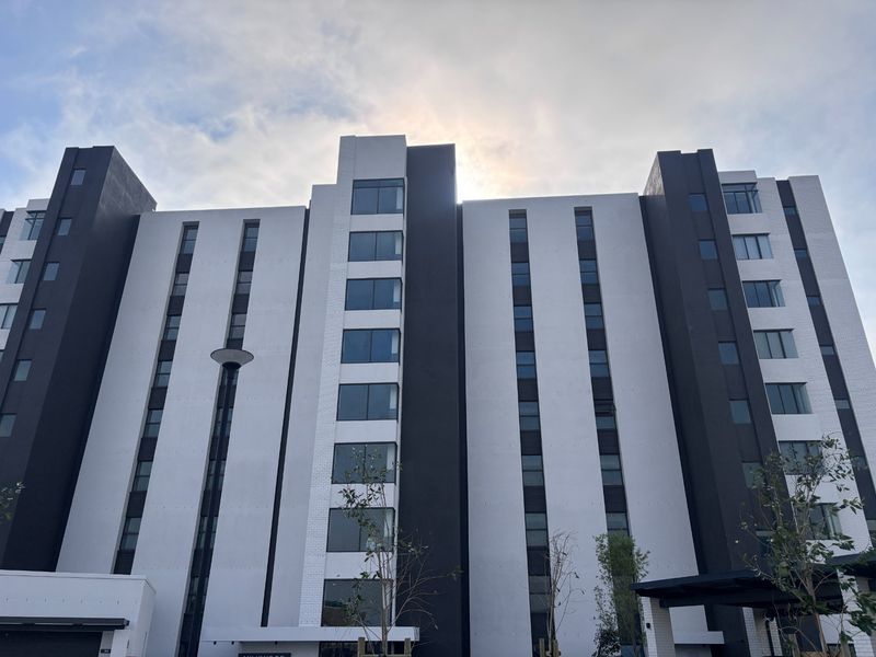 A modern multi-story apartment building facade featuring a contemporary design with contrasting white and dark grey finishes and large windows.
