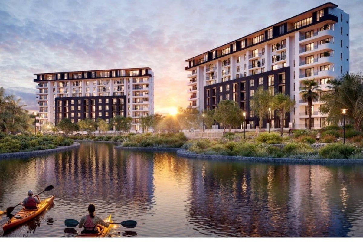 A scenic view of modern multi-story apartment buildings situated along a landscaped waterfront, featuring balconies and well-maintained outdoor communal areas.