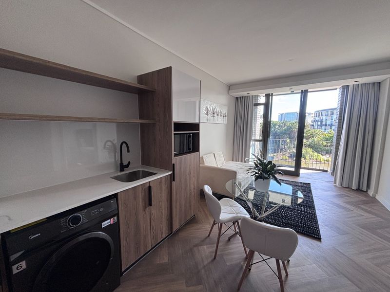 Modern open-plan apartment featuring herringbone timber flooring, a sleek kitchenette with stone countertops, and direct access to a private balcony.