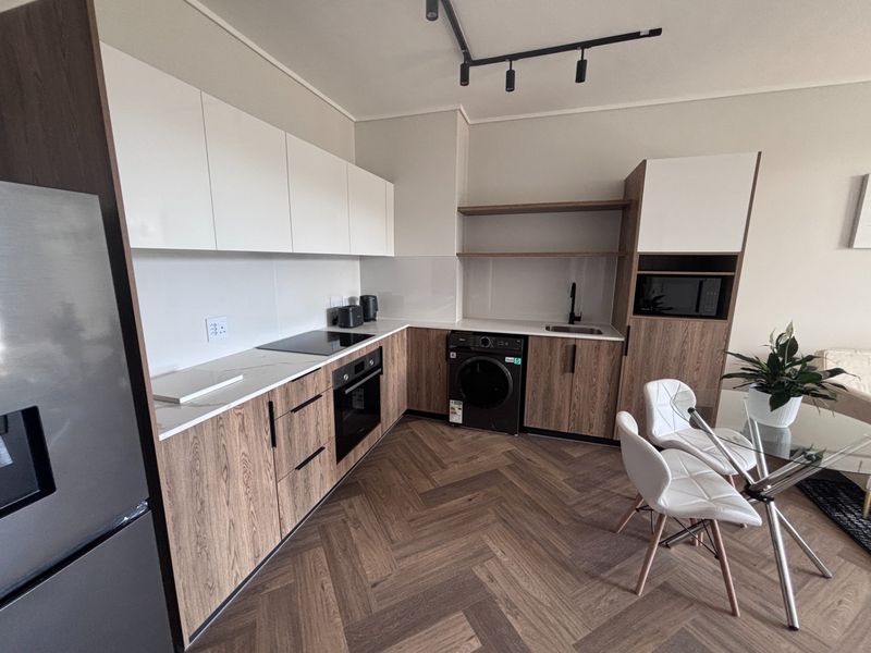 Modern kitchen featuring wood-grain cabinetry, white stone countertops, integrated appliances, herringbone flooring, and contemporary track lighting.