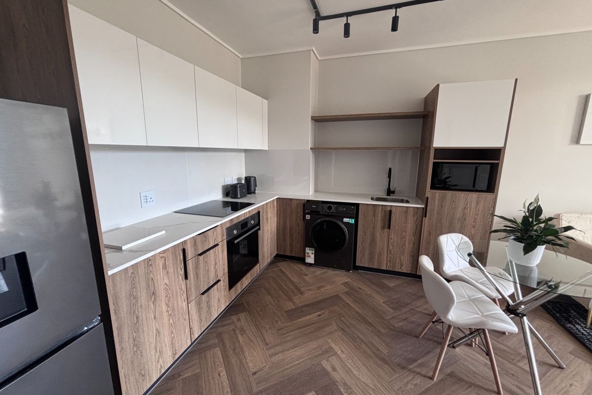Modern kitchen featuring wood-grain cabinetry, white stone countertops, integrated appliances, herringbone flooring, and contemporary track lighting.
