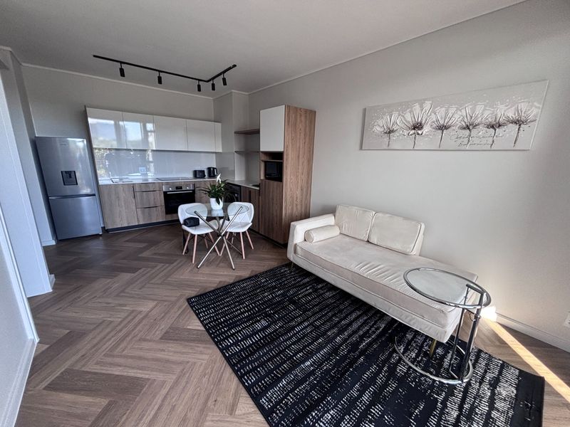 Modern open-plan living area featuring high-quality herringbone flooring, sleek contemporary kitchen cabinetry, and integrated appliances in a bright, well-maintained space.