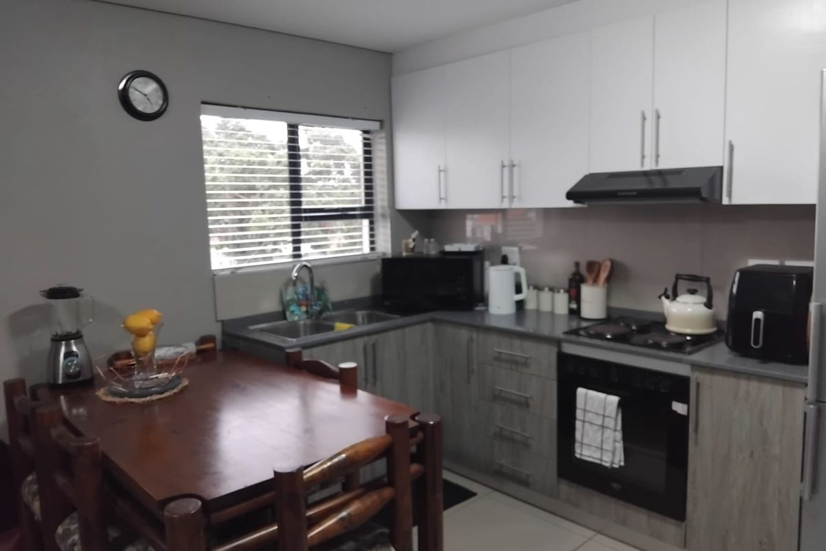A functional kitchen featuring modern two-tone cabinetry, a built-in oven with gas hob, extractor fan, and a stainless steel sink with a window view.