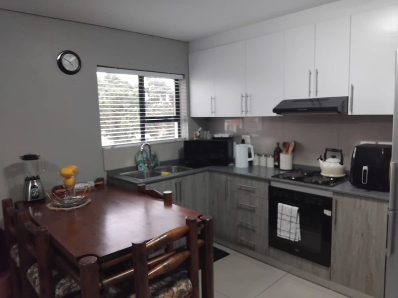 A functional kitchen featuring modern two-tone cabinetry, a built-in oven with gas hob, extractor fan, and a stainless steel sink with a window view.