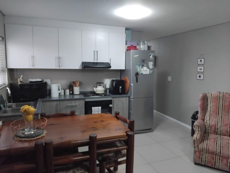 Open plan kitchen and living area featuring white cabinetry, built-in appliances, and neutral tiled flooring.