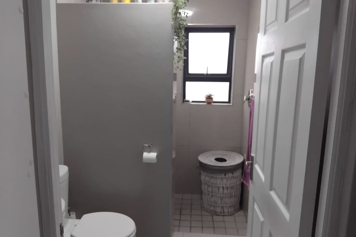 A compact bathroom featuring a toilet, tiled flooring, and a partition wall, providing a functional layout with natural light from the window.