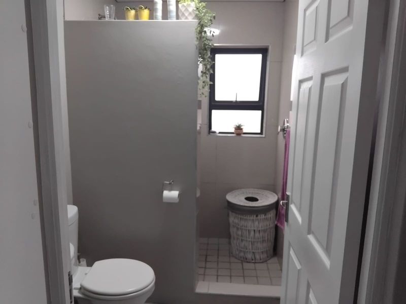 A compact bathroom featuring a toilet, tiled flooring, and a partition wall, providing a functional layout with natural light from the window.