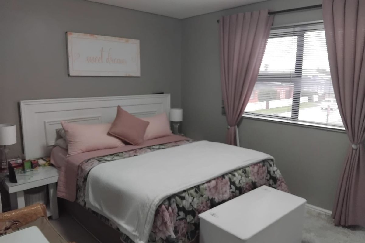 A well-maintained bedroom featuring neutral grey walls, a large window with pink curtains, and ample space for a double bed.