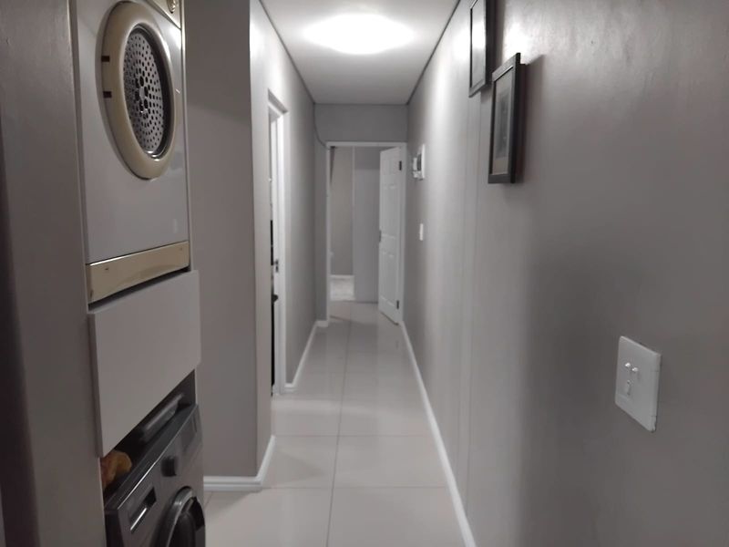 A clean, well-lit hallway featuring tiled flooring and a convenient built-in stacked laundry area, providing efficient use of space.