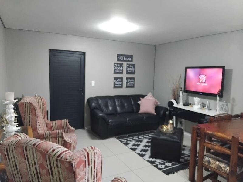 A living room area featuring neutral tiled flooring, grey walls, and a central ceiling light fixture.