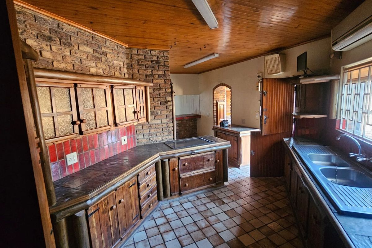 A rustic kitchen featuring timber cabinetry, exposed brick walls, tiled countertops, and a timber ceiling, offering a dated aesthetic with potential for modernization.