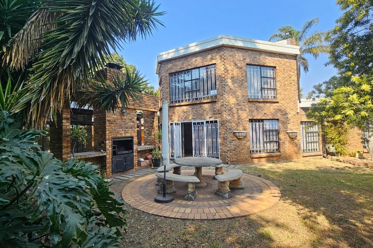 Rear view of a face brick house featuring a paved patio area with a built-in braai and established garden surroundings.