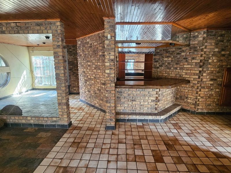 A spacious interior area featuring a built-in brick bar, timber-clad ceiling, and tiled flooring, offering a rustic aesthetic with potential for modernization.