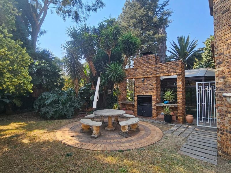 Outdoor entertainment area featuring a built-in brick braai, circular paved seating area with fixed stone furniture, and established garden surroundings.