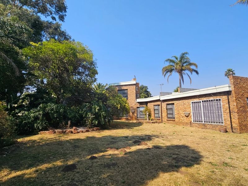 A view of the rear face brick facade of the house, featuring security bars on windows and a large, established garden area.