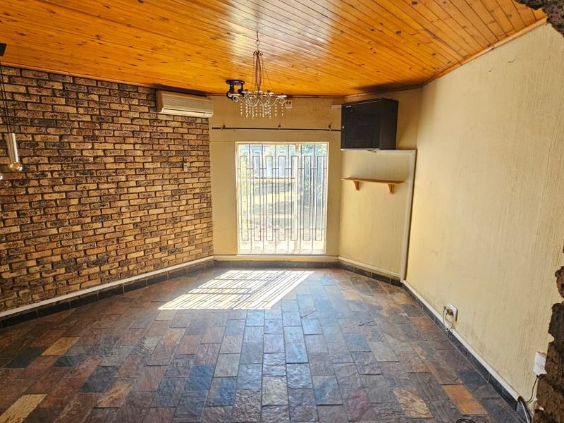 An empty living room featuring a rustic exposed brick wall, slate tile flooring, and a timber-clad ceiling with a central light fixture.