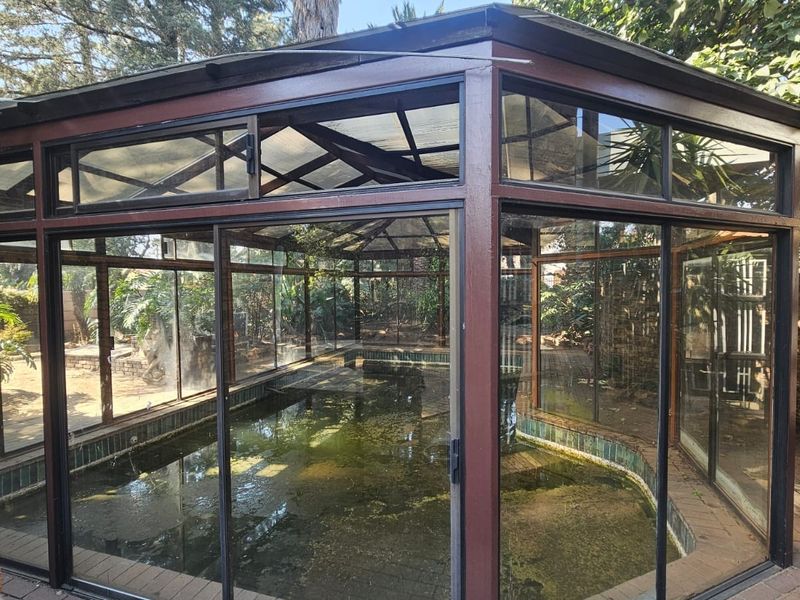 An enclosed swimming pool structure featuring a metal frame with sliding glass doors, set within a paved garden area.