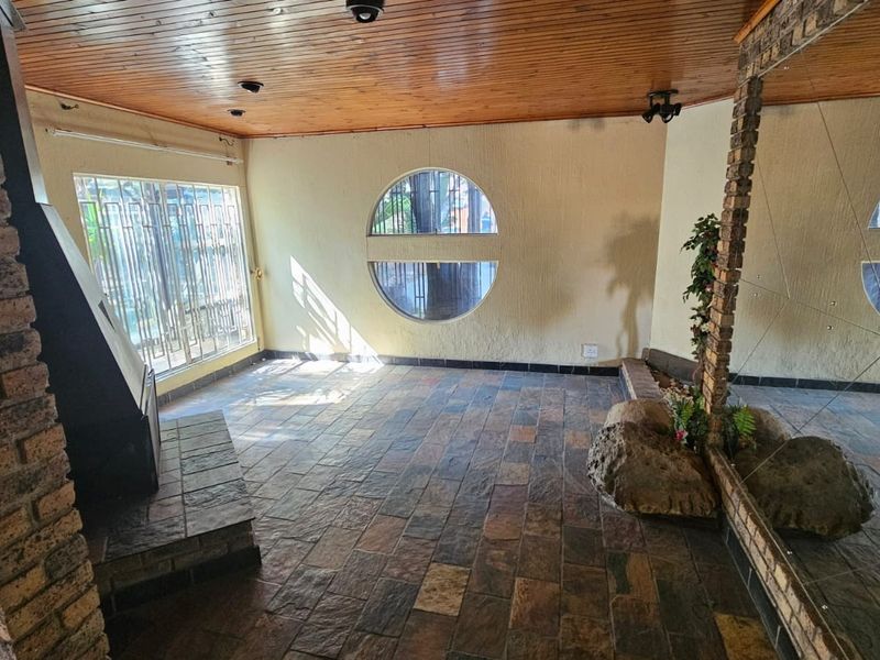 Spacious living area featuring a timber ceiling, slate tile flooring, a brick fireplace, and a unique circular window, offering a rustic aesthetic.