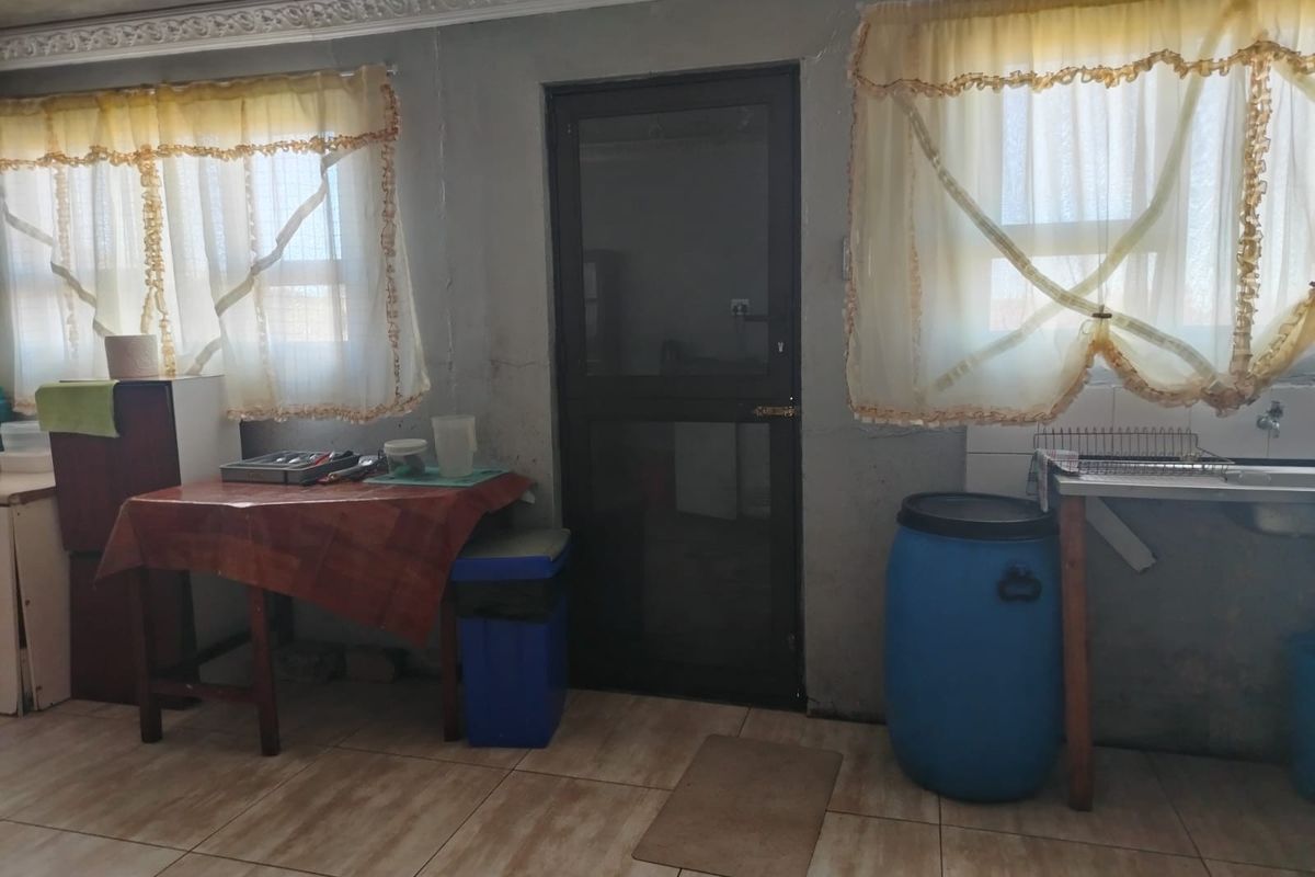 A functional kitchen area featuring tiled flooring, a sink, and a screen door, requiring cosmetic updates to the wall finishes.
