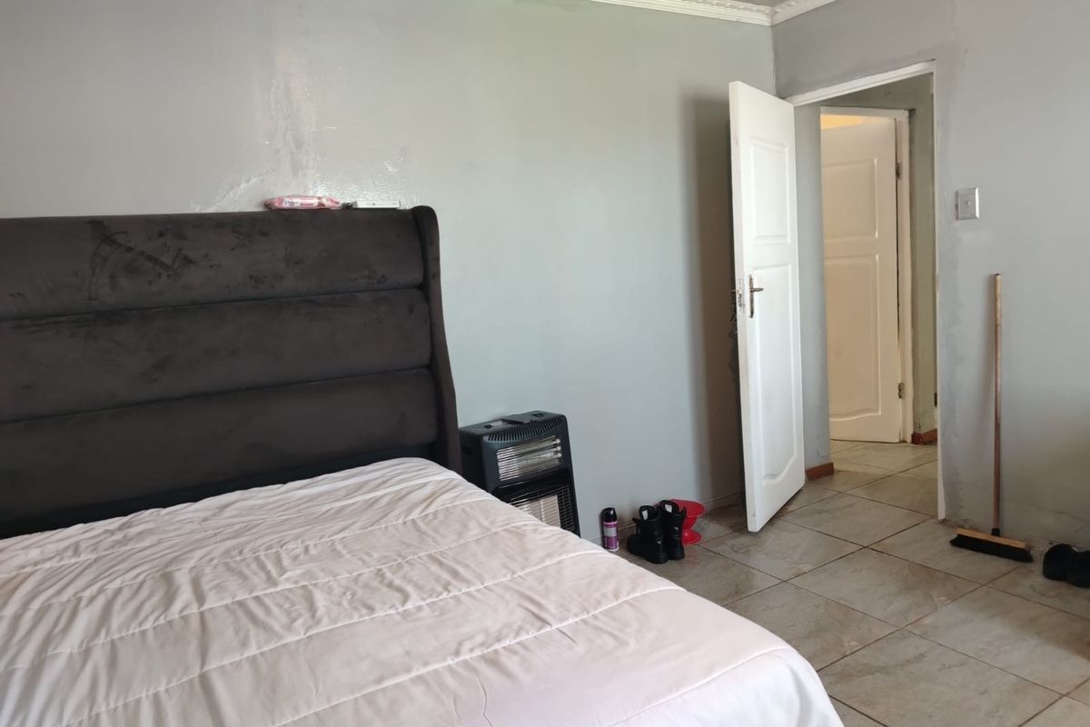 A bedroom featuring tiled flooring and ceiling cornice, showing signs of wall surface wear and water staining.